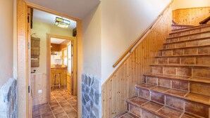 A wooden staircase leading to a second floor, a kitchen area with a hanging basket, and a stone wall.