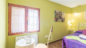 Une pièce avec un lit, une table sur laquelle se trouve une carafe, un radiateur et une fenêtre avec des rideaux.