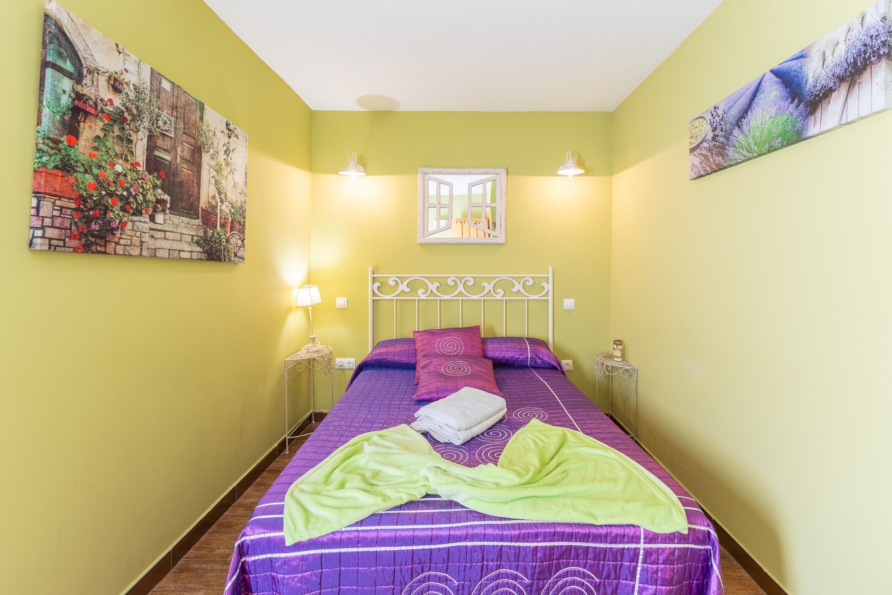 Una habitación con una cama, una mesita de noche, una lámpara, un cuadro y una ventana.