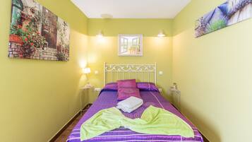 Una habitación con una cama, una mesita de noche, una lámpara, un cuadro y una ventana.