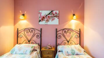 Un dormitorio con dos camas, cada una con ropa de cama estampada, una mesita de noche con lámpara y un cuadro de flores colgado en la pared.