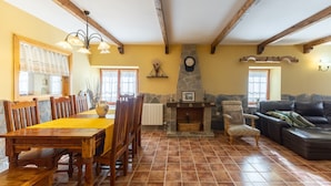 A dining area with a wooden table and chairs, a stone fireplace, a sofa, and a clock on the wall.