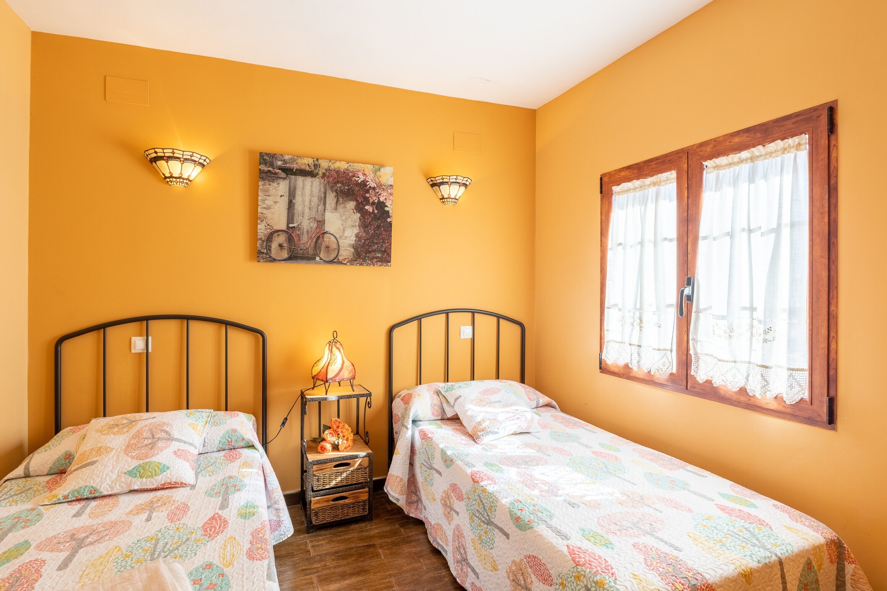 Een kamer met twee bedden, een wandlamp, een schilderij en een raam met gordijnen.