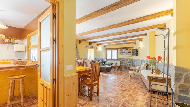 A spacious kitchen with a dining area, wooden beams, and a stone wall.