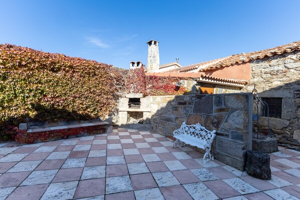 A courtyard with a checkered floor, a stone bench, and a stone wall with a chimney.