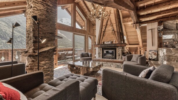 A spacious living area with a stone fireplace, modern furniture, and large windows offering mountain views. - Magnificent traditional 4 bedroom farmhouse a walk from Chamonix centre (Chamonix)