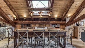 A rustic wooden dining area with a high ceiling and exposed beams, featuring a central table with chairs and pendant lighting. - Magnificent traditional 4 bedroom farmhouse a walk from Chamonix centre (Chamonix)