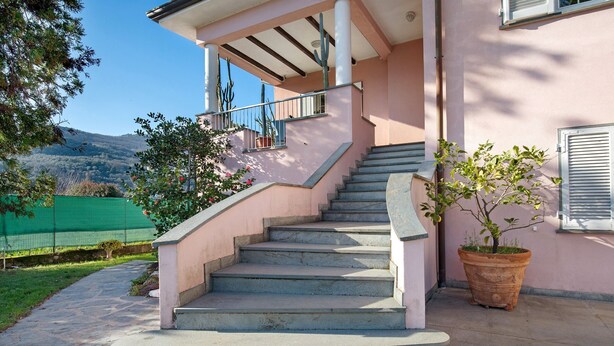 Eine Treppe führt zu einem Gebäude mit einer rosa Fassade, einem Blumentopf und Blick auf eine grüne Landschaft.