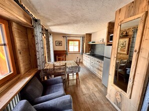 A cozy cabin interior with a dining table, chairs, a sofa, a kitchen area, and a large mirror.