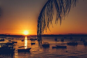 A sunset over a calm body of water with several boats anchored. - Pousada Biônica (Cairu)