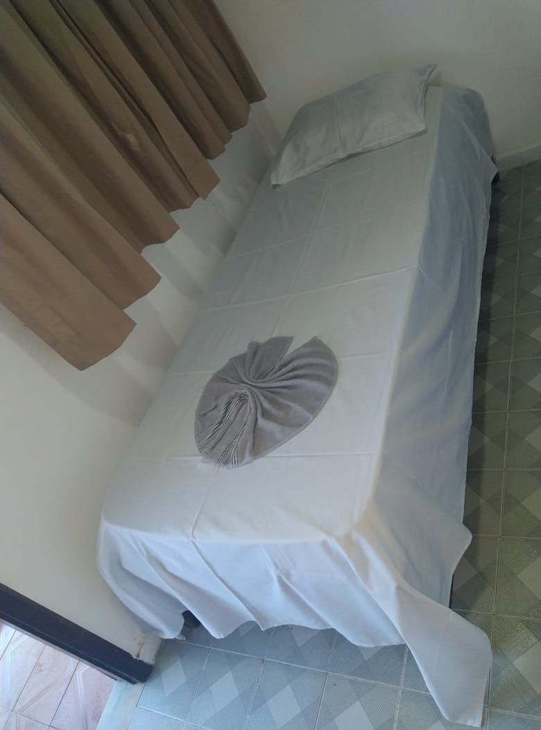Uma cama de solteiro com um edredom branco e uma almofada decorativa.