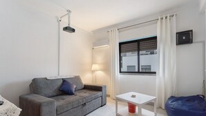 Ein modernes Wohnzimmer mit einem grauen Sofa, einem weißen Couchtisch, einem blauen Sitzsack, einer Lampe und einem Fenster mit Vorhängen.