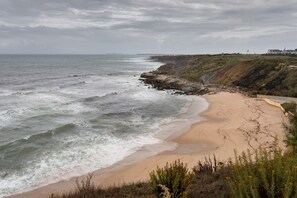 A coastal landscape with a sandy beach, rocky cliffs, and a distant building.