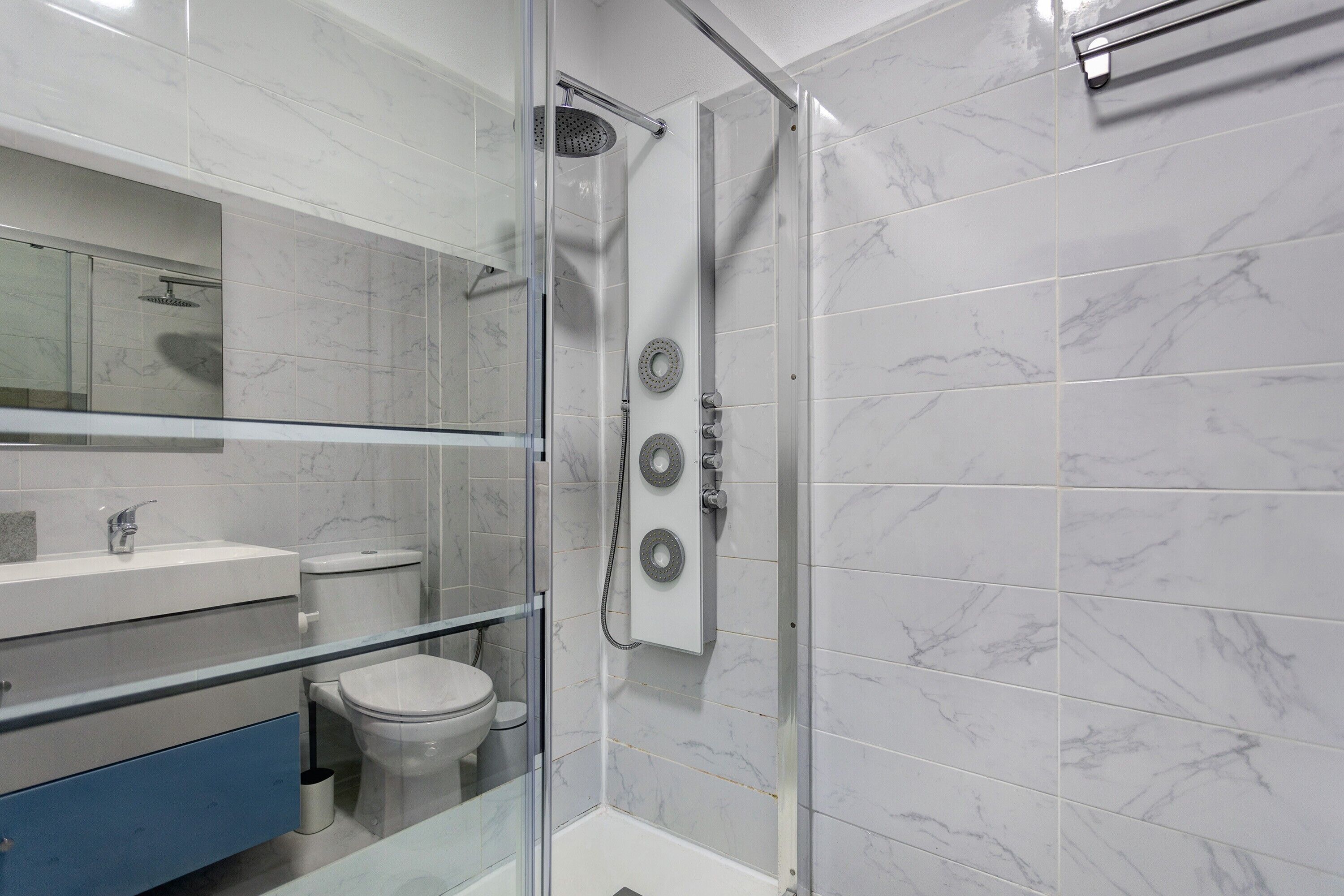 A modern bathroom with a glass shower enclosure, a toilet, a sink, and a mirror.