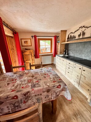 A rustic kitchen with wooden cabinets, a black countertop, and a table with a patterned tablecloth.