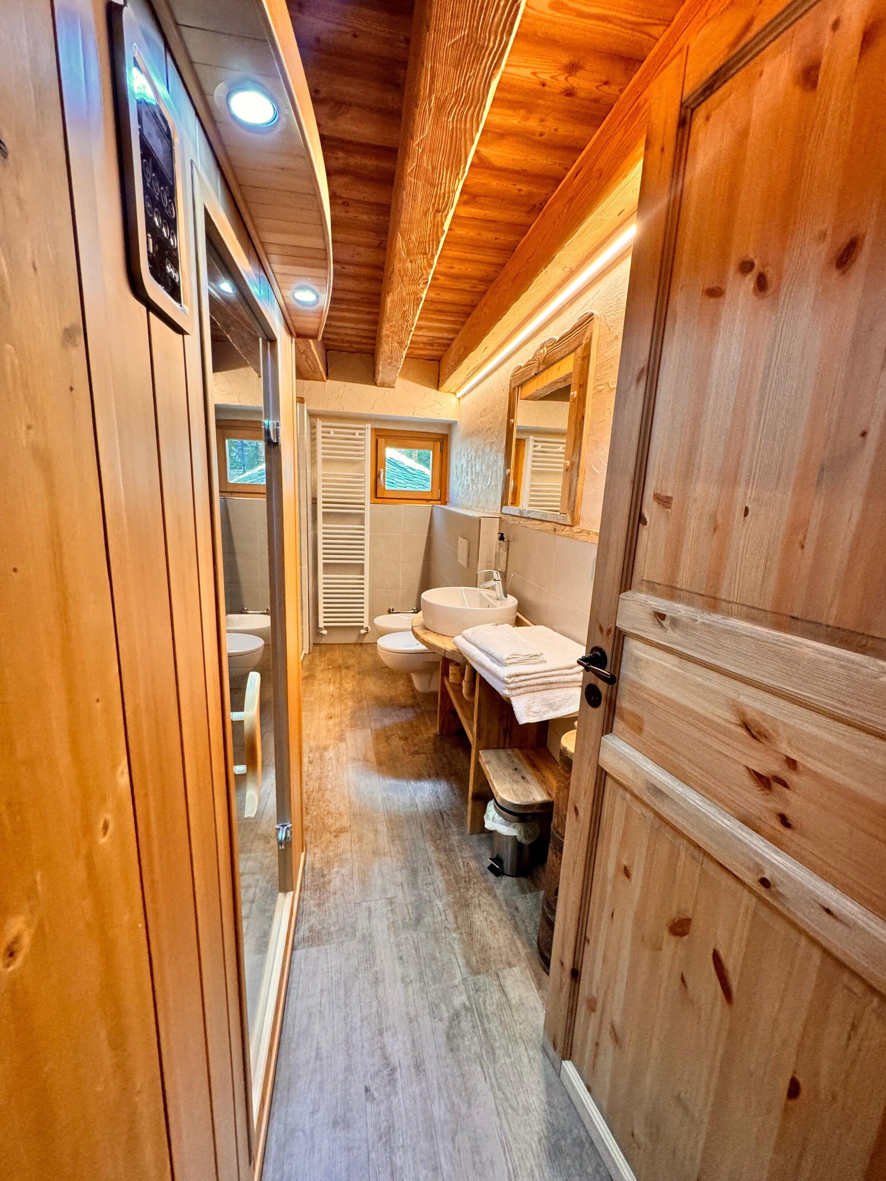 Ein schmaler Holzkorridor, der zu einem Badezimmer mit Toilette, Waschbecken und Spiegel führt.