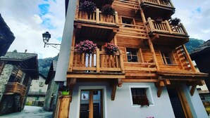 Un immeuble en bois à plusieurs étages, doté de balcons, avec un banc à l’extérieur et une chaîne de montagnes en arrière-plan.