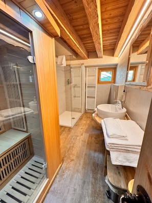 A wooden cabin bathroom with a glass shower enclosure, a sink, and a mirror.