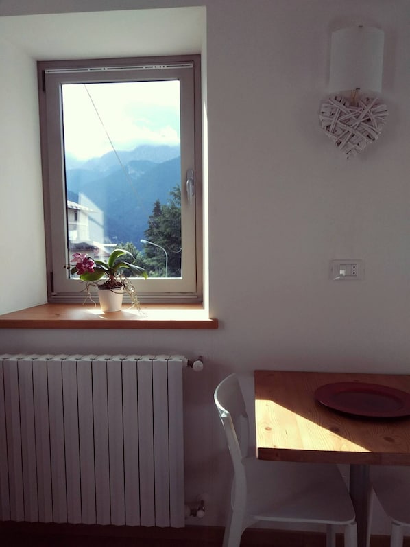 A room with a window overlooking mountains, a radiator, a wooden table, and a white chair.