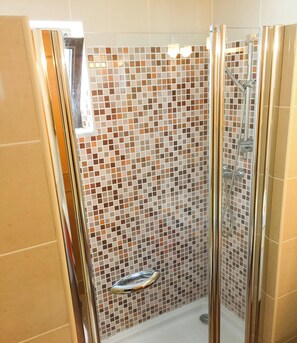 Une douche avec une porte en verre, des murs carrelés et un pommeau de douche chromé.