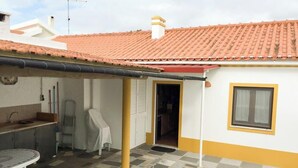 A residential building with a tiled roof, a covered patio area, a kitchen with a sink, and a window with a yellow frame. - Cottage 'Casas Da Lagoa - T2 Sul' with Private Garden, Balcony and Wi-Fi (Brescos)