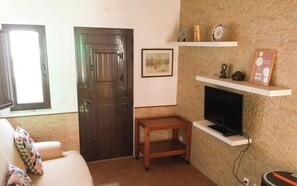 Un salon avec une porte en bois foncé, un canapé blanc, une petite table en bois, une cheminée et un téléviseur fixé au mur.