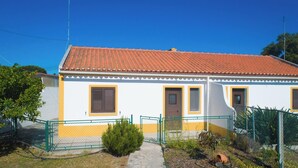 A two-story building with a red-tiled roof, a small front garden, and a green fence. - Cottage 'Casas Da Lagoa - T2 Sul' with Private Garden, Balcony and Wi-Fi (Brescos)