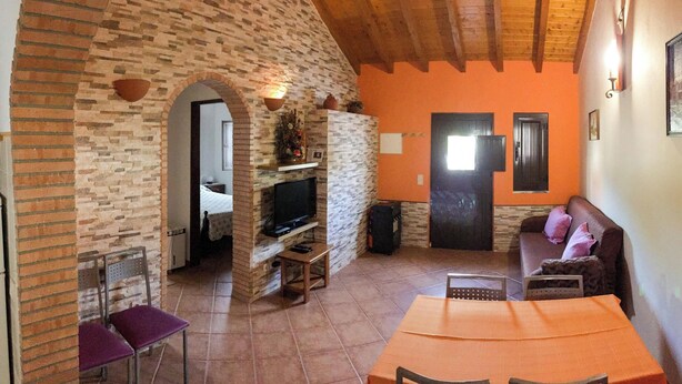 Un salon avec un mur en pierre, un téléviseur, un canapé et une table à manger.