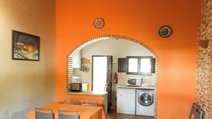 Un coin repas avec une table et des chaises, un arc donnant accès à une cuisine équipée d’un lave-linge et d’un four à micro-ondes.
