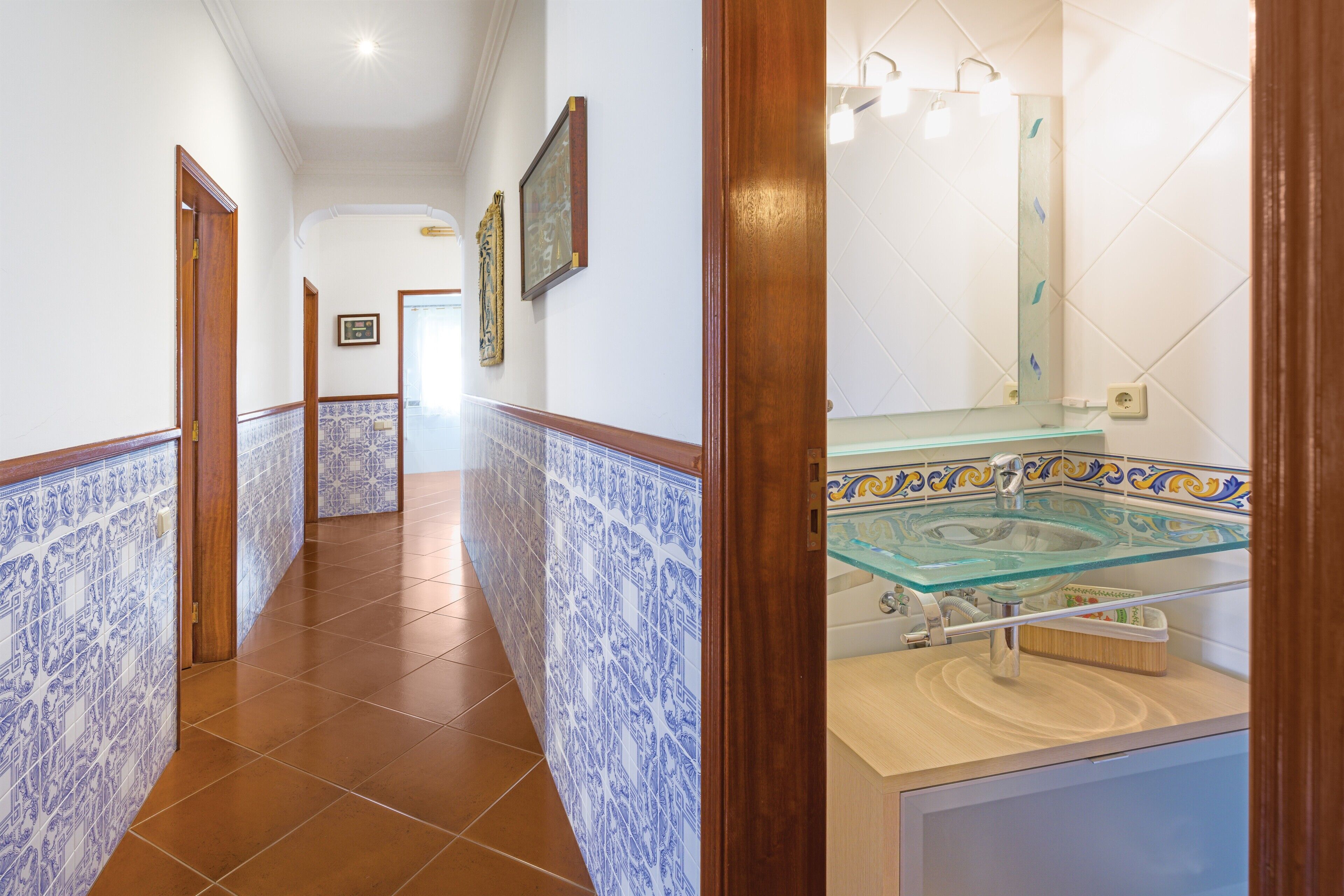 Un pasillo con baldosas estampadas, un lavabo de cristal y un marco de puerta de madera.