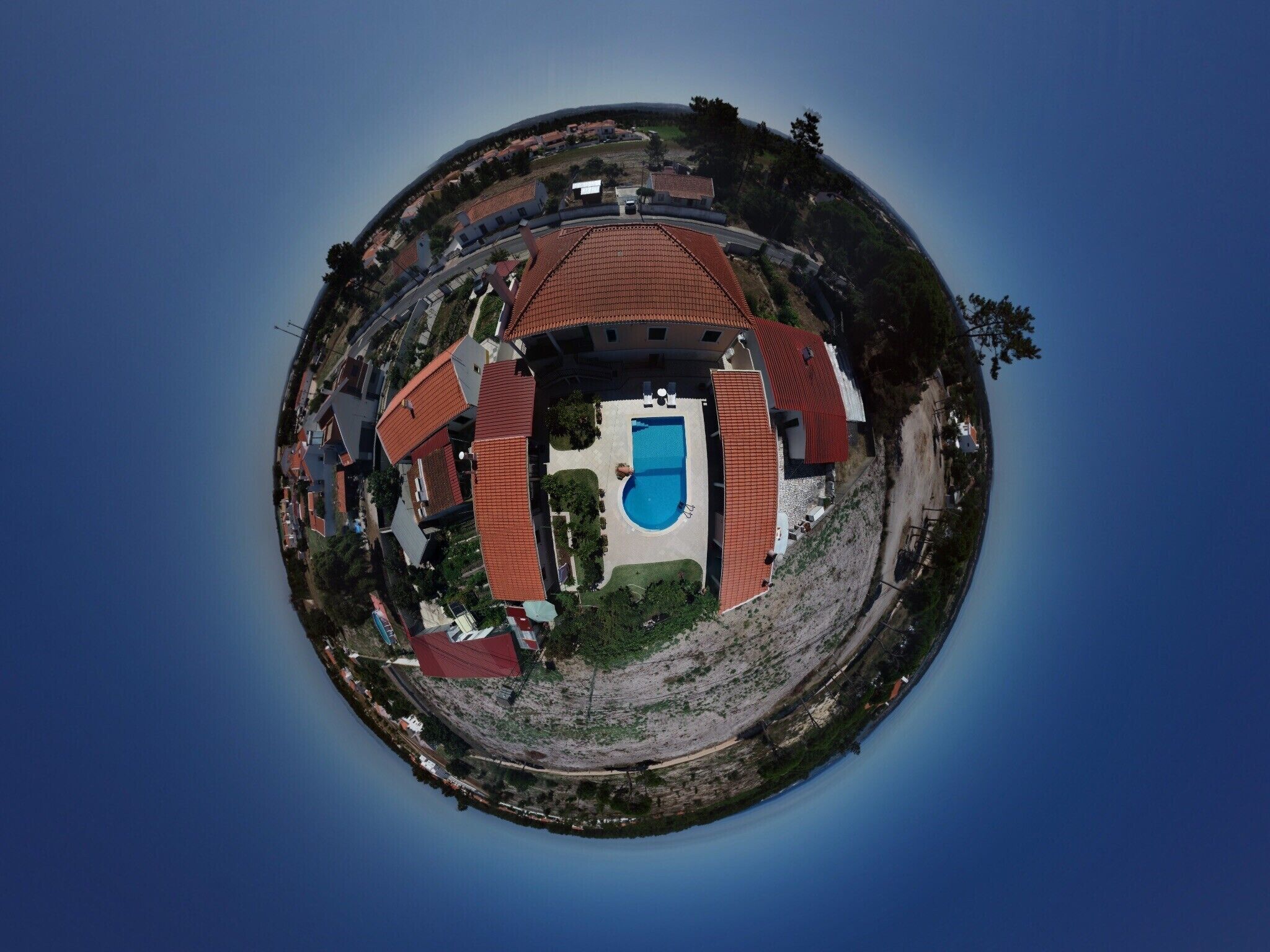 A circular aerial view of a property with a swimming pool, multiple buildings, and a surrounding landscape.