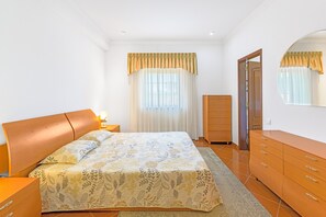 Un dormitorio con cama, cómoda, espejo y ventana con cortinas.