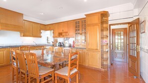 A spacious kitchen with wooden cabinets, a dining table with chairs, and a tiled floor. - Villa 'Beautiful Deluxe 4 Bedroom' with Private Pool, Garden & Wi-Fi (Brescos)