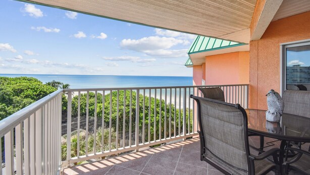 Un balcon avec vue sur la mer, une table avec des chaises et une statue d’oiseau.
