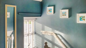 Une pièce avec un mur bleu foncé, une fenêtre avec des stores, un plancher en bois et une rambarde blanche.