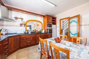 Cozinha com armários de madeira, forno embutido e área de jantar com mesa posta para dois.