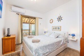Quarto com cama, mesa de cabeceira, televisão, janela com cortinas e vista para o exterior.