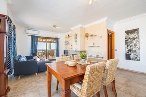 Uma sala de estar moderna com uma mesa de jantar de madeira, cadeiras de vime, um sofá e uma televisão.