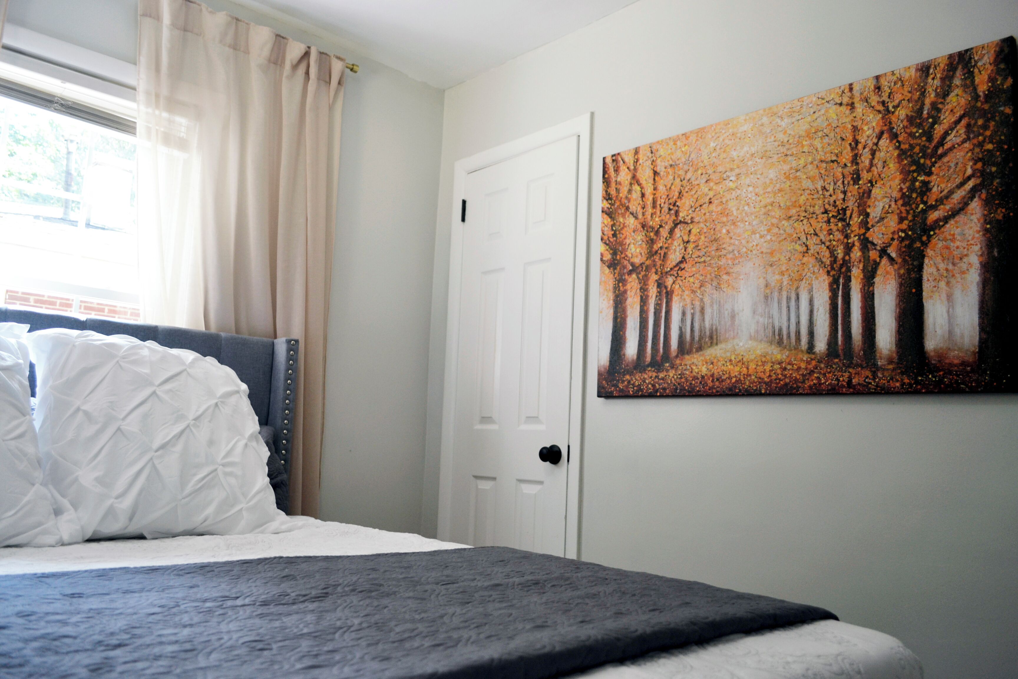 A bedroom with a bed, a door, and a painting of trees.