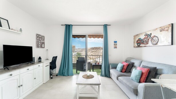 Una sala de estar moderna con un televisor de pantalla plana, un sofá con cojines de colores, una mesa de centro y un balcón con vistas.