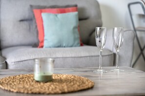 Una sala de estar con un sofá gris, una almohada azul y roja, dos vasos transparentes y un pequeño recipiente de vidrio sobre un posavasos tejido.