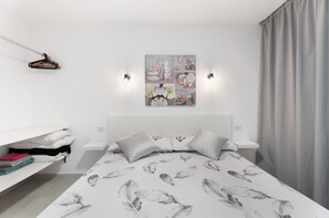 A modern bedroom with a bed, pillows, a wall-mounted light fixture, and a painting.