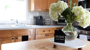 Een keuken met houten kastjes, een wit aanrechtblad en een vaas met witte bloemen op een witte standaard.