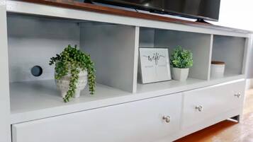 Un meuble blanc pour télévision, avec un téléviseur à écran plat posé dessus, trois tiroirs et deux plantes en pot.