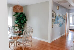 Un comedor con mesa de vidrio y sillas de mimbre, una lámpara colgante y un mural en la pared.