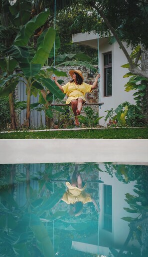 Una persona en un columpio dentro de un jardín con piscina.