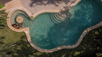 Una piscina grande de forma irregular con un elemento circular en el centro y una cubierta perimetral.