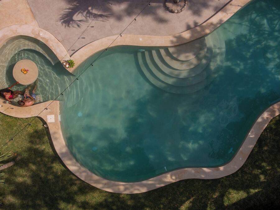 Una piscina grande de forma irregular con un elemento circular en el centro y una cubierta perimetral.