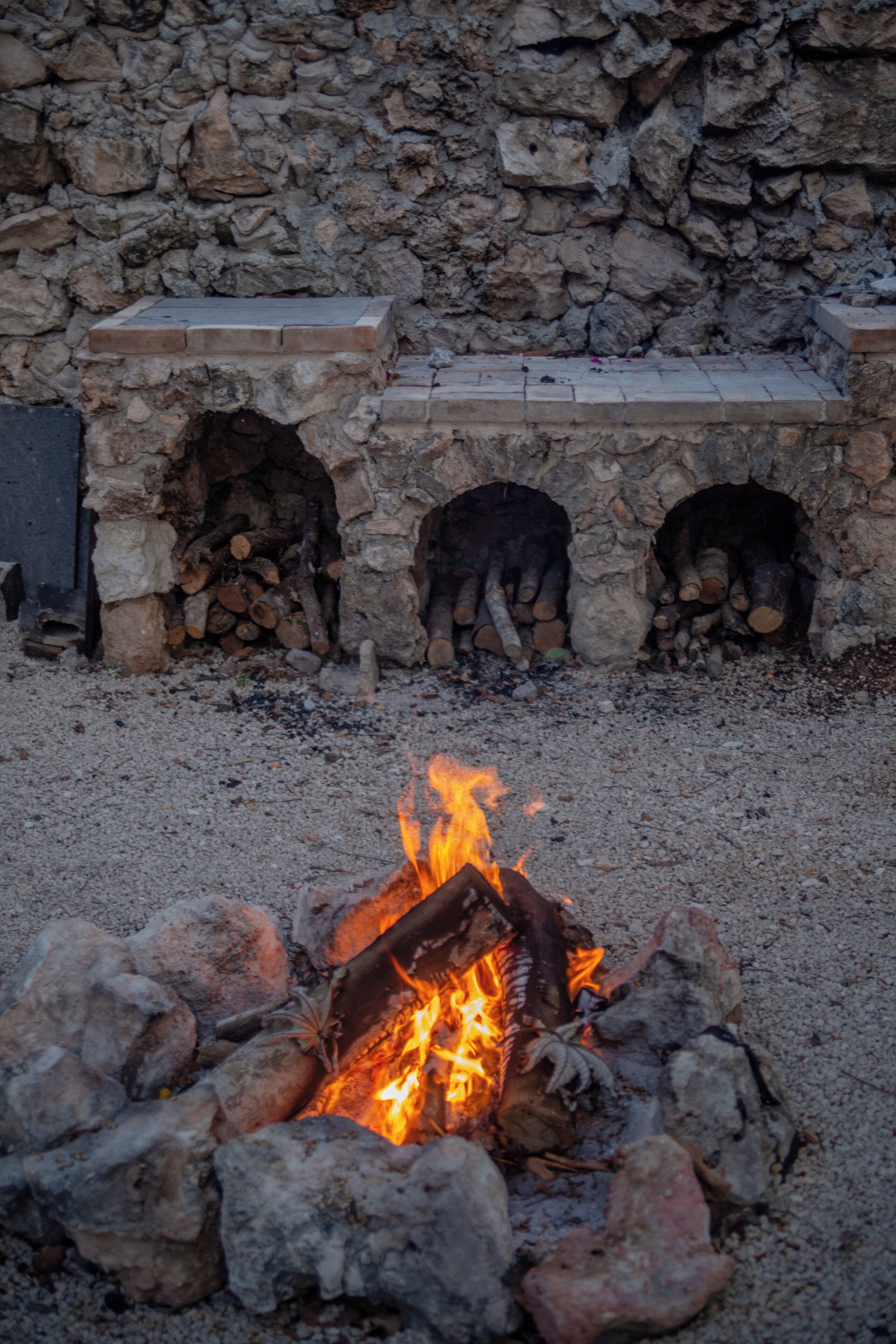 A stone fireplace with logs burning, surrounded by a stone wall.