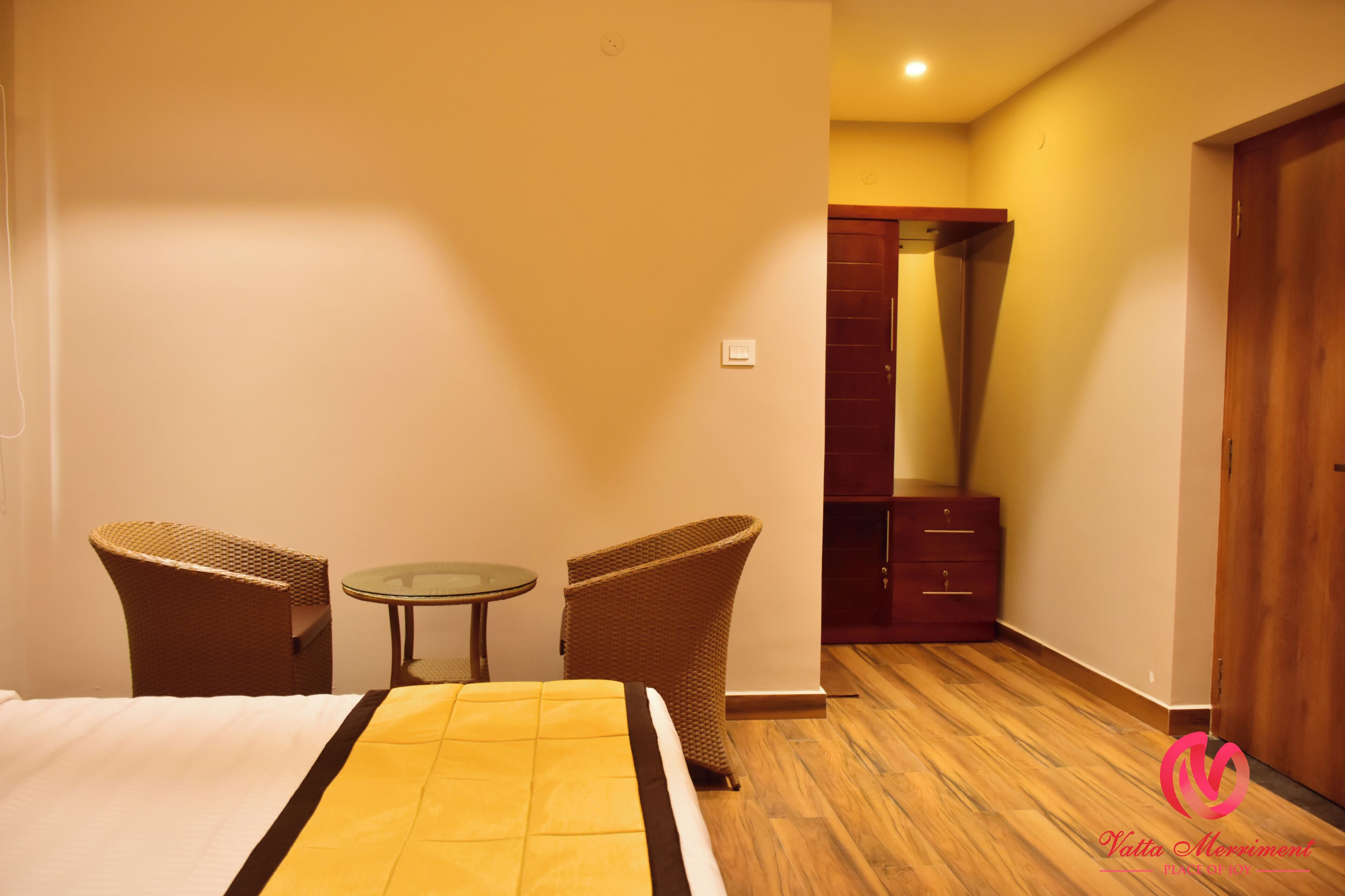 A hotel room with a bed, two wicker chairs, a small table, and a wooden wardrobe.